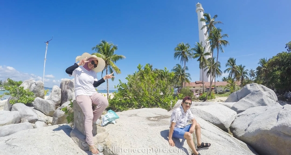 Pasangan berdiri di pantai Belitung latar belakang mercusuar pulau lengkuas